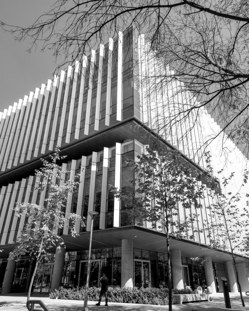 Black and white photo of a modern office building with trees and people walking nearby.
