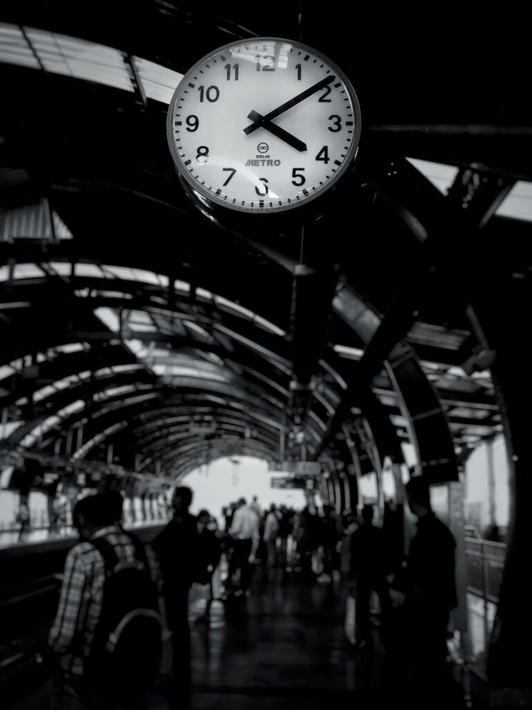 Black and white photo of a bustling metro station with a prominent clock and commuters.